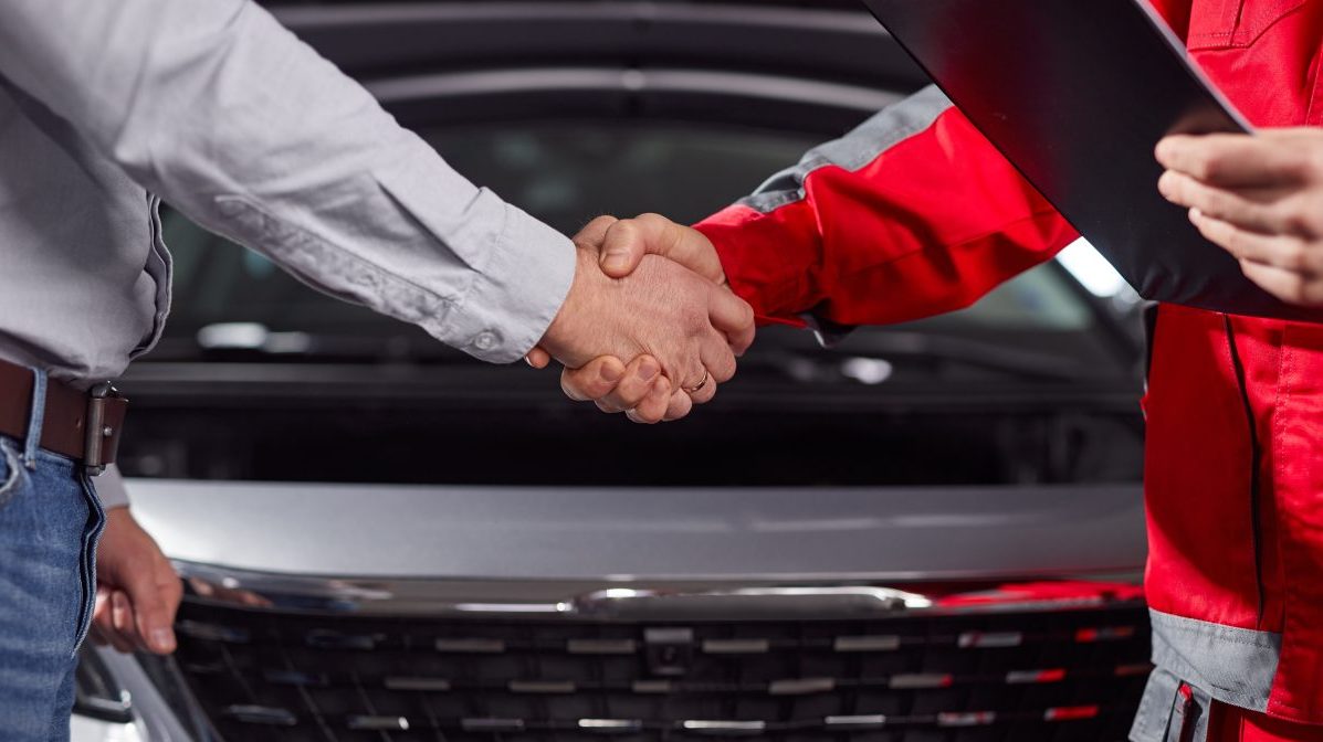 Two men shaking hands in front of an automotive franchise car.