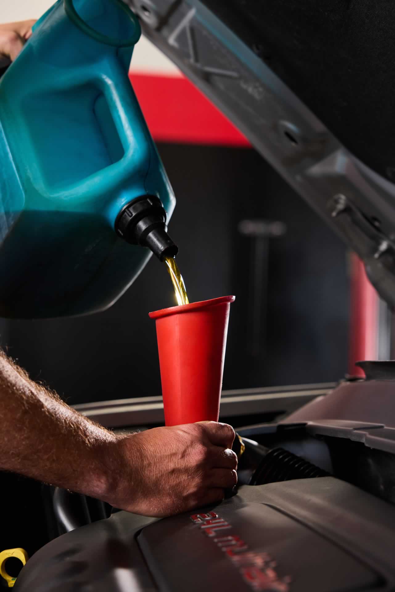 Person pouring engine oil into a car's oil compartment using a red funnel.