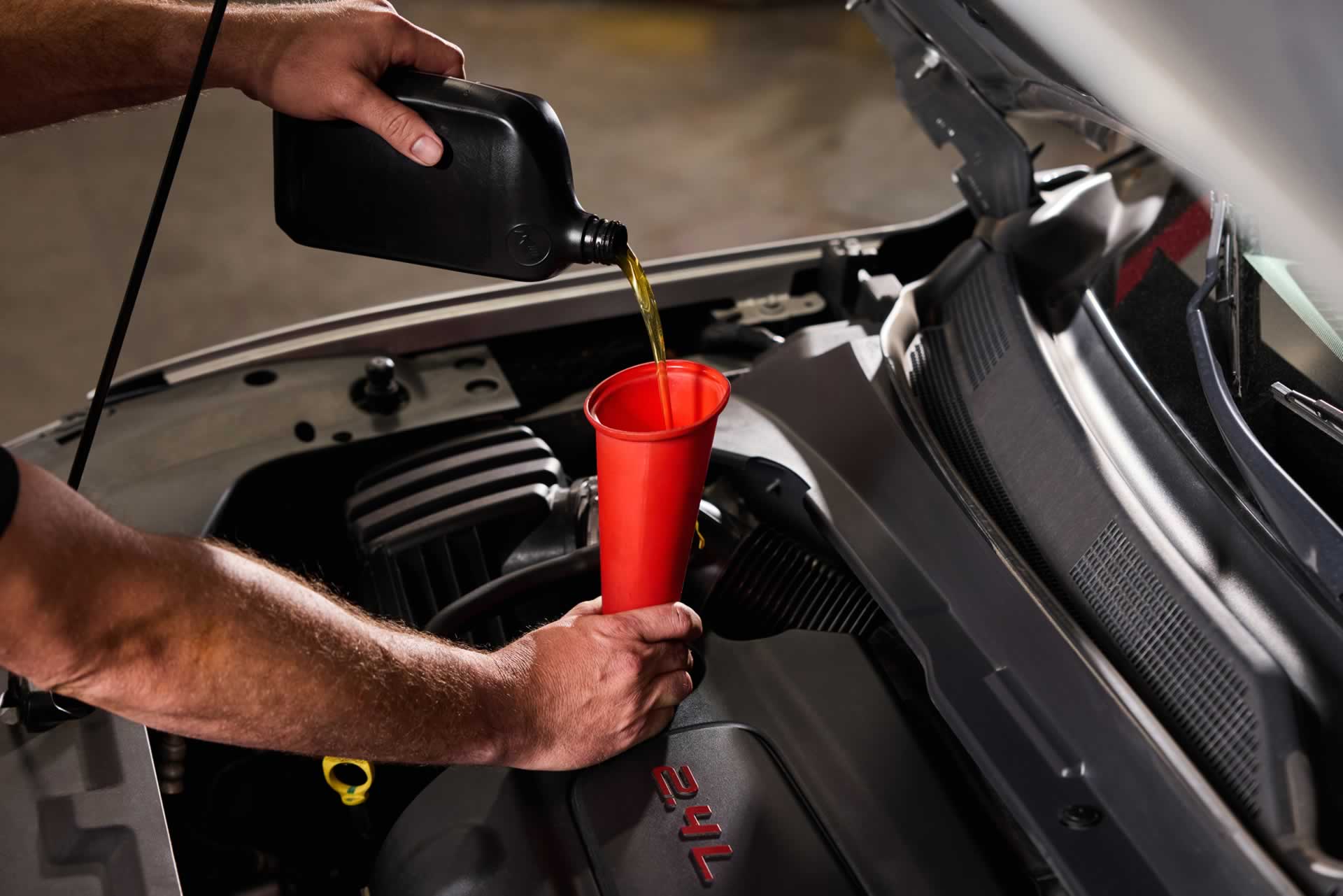 Person pouring motor oil into a funnel placed in a car engine.