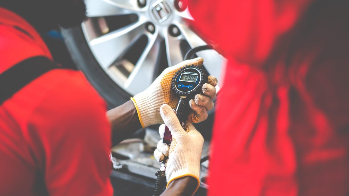 An automotive franchise mechanic is checking the tire pressure of a car.