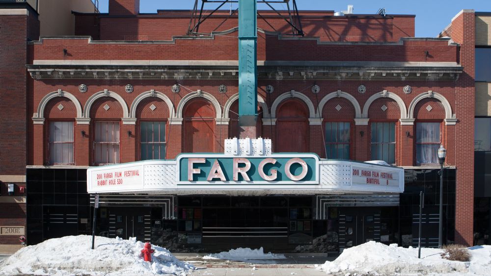 An old theater with a marquee that reads "Fargo" in large letters, symbolizing its franchise income potential, with snow piled up in front of it.