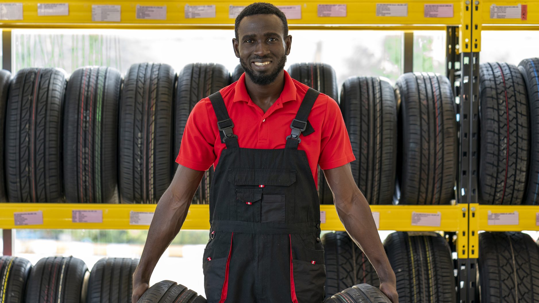 A man in overalls standing in front of a tire rack at an automotive franchise.