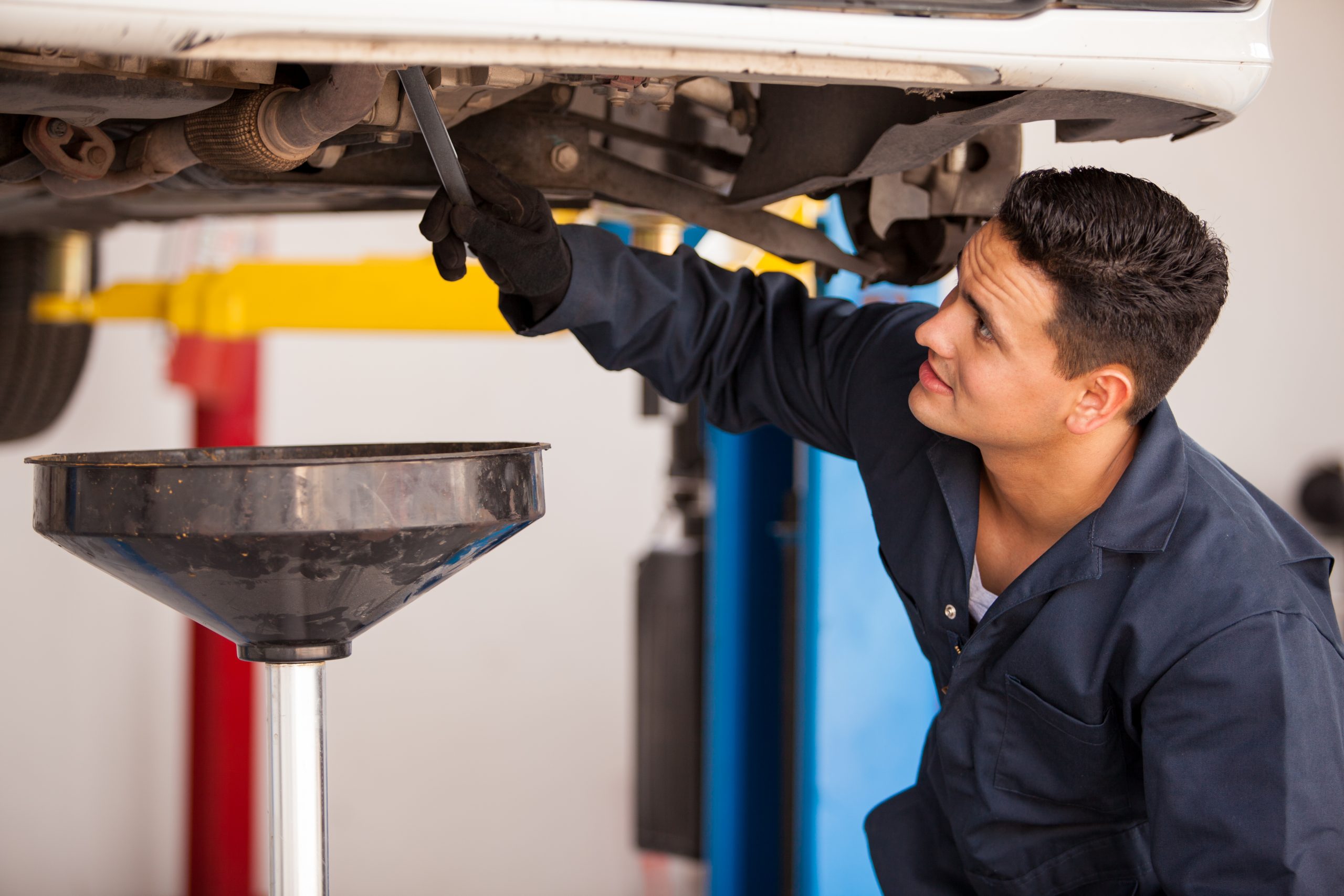 A mechanic from an automotive franchise is working underneath a car.