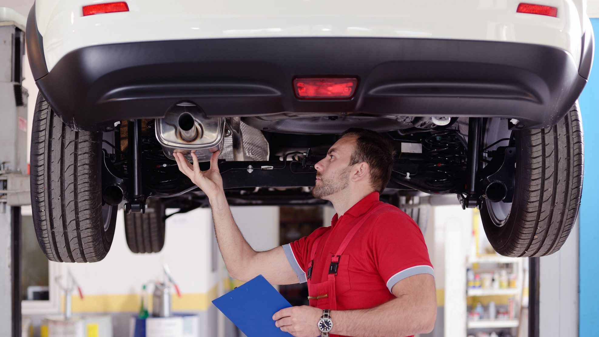 A mechanic inspecting the underside of a car at an automotive franchise.