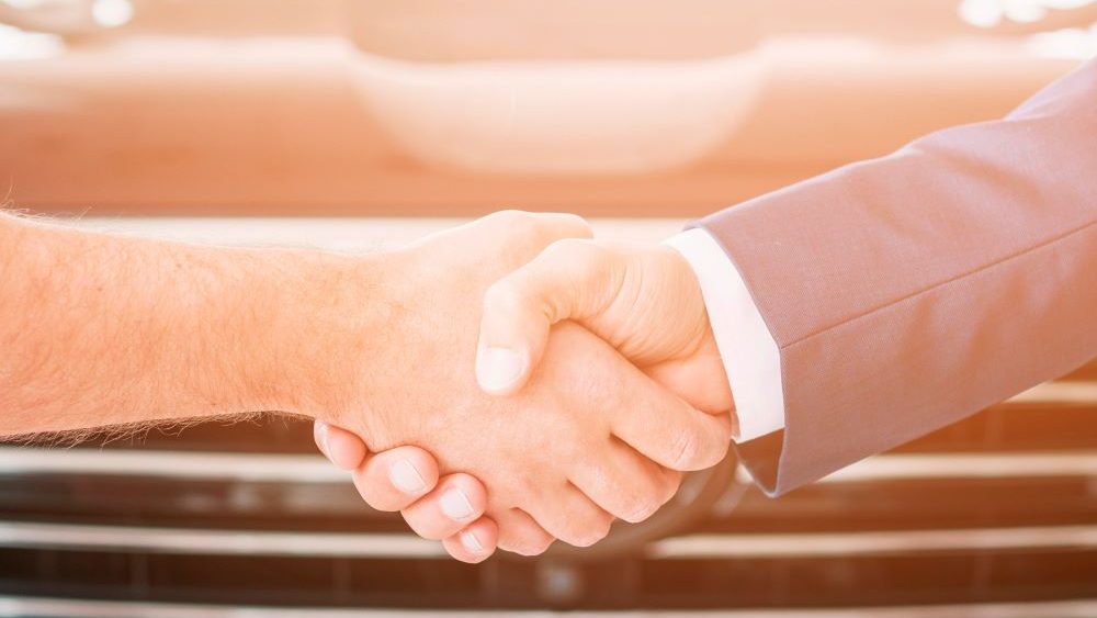 Two men shaking hands in front of an automotive franchise.