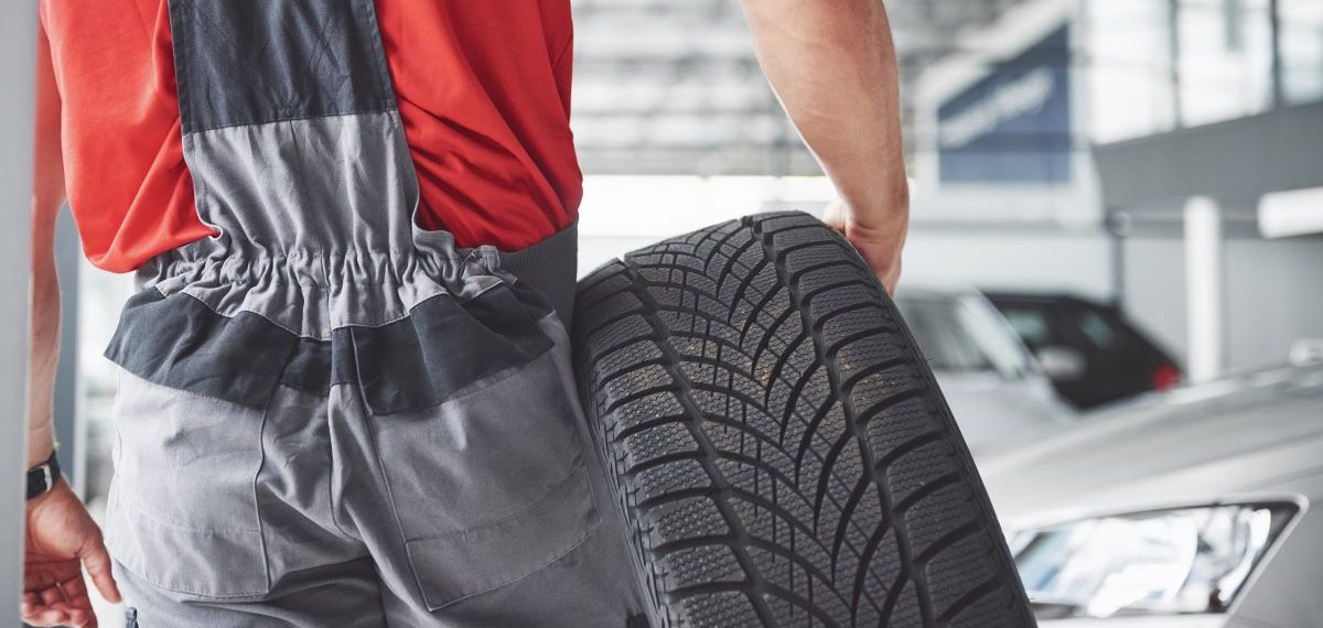 A man in overalls is holding a tire in an automotive showroom.
