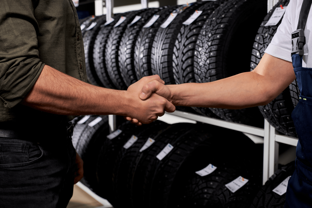 Two men shaking hands in front of tire racks at an automotive franchise.